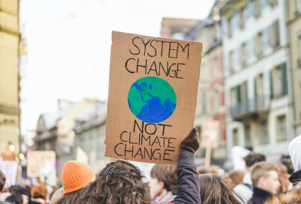 A demonstrator holds up a cardboard sign with a painted planet earth on it. It read 'System Change not Climate Change'