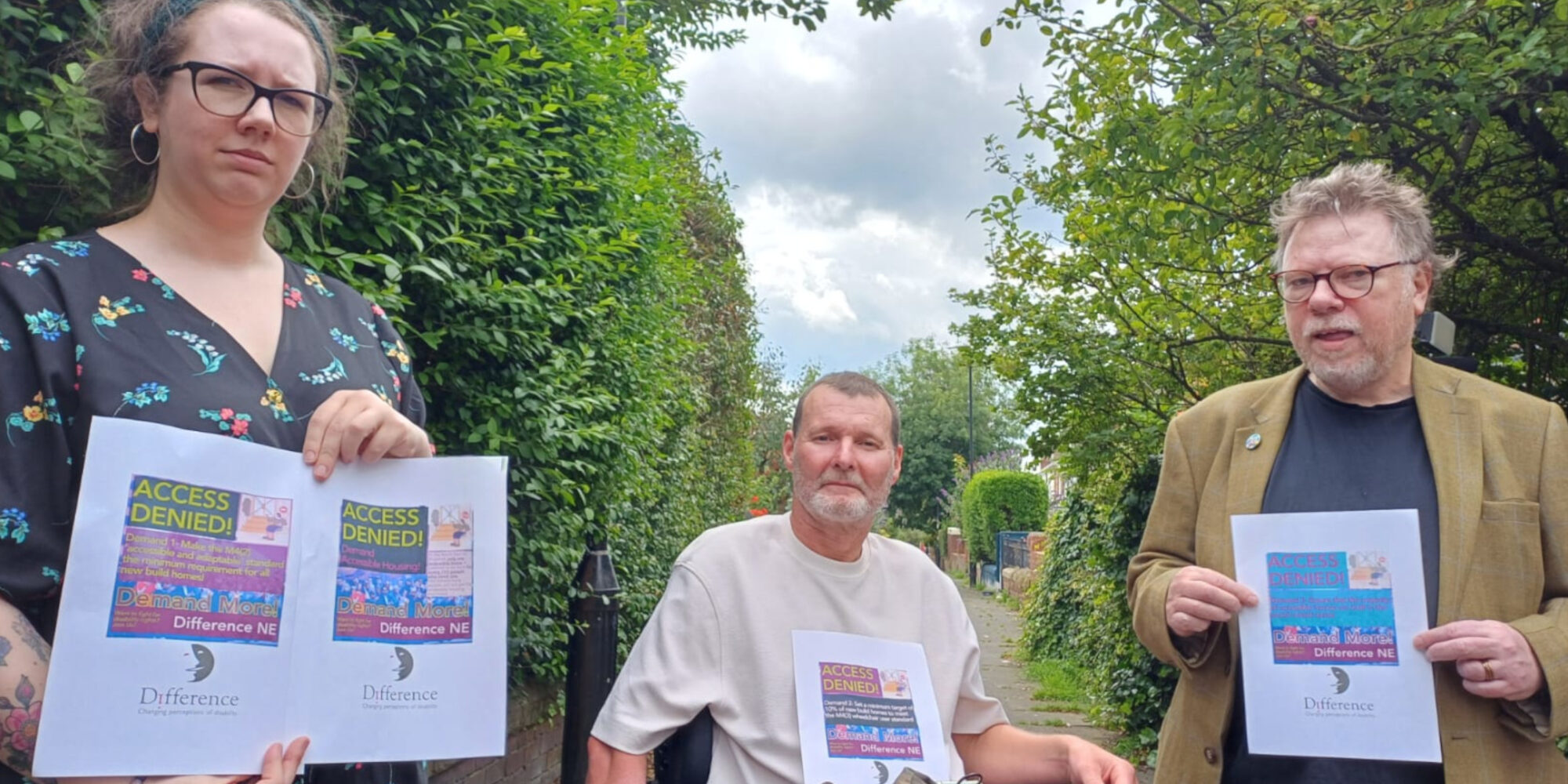 Three people hold up flyers with images and text on, the words "Access Denied" are visible on each.