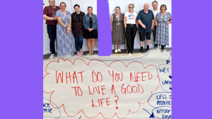 Hartlepool Disability Rights: A group of twelve people stand together, smiling, in front of a white wall at an indoor event. They are of varying ages and genders, some using mobility aids. Below the group, a large handwritten poster reads in red letters: “WHAT DO YOU NEED TO LIVE A GOOD LIFE?” Blue writing surrounds the question, with arrows and ideas partially visible, suggesting a brainstorming session.