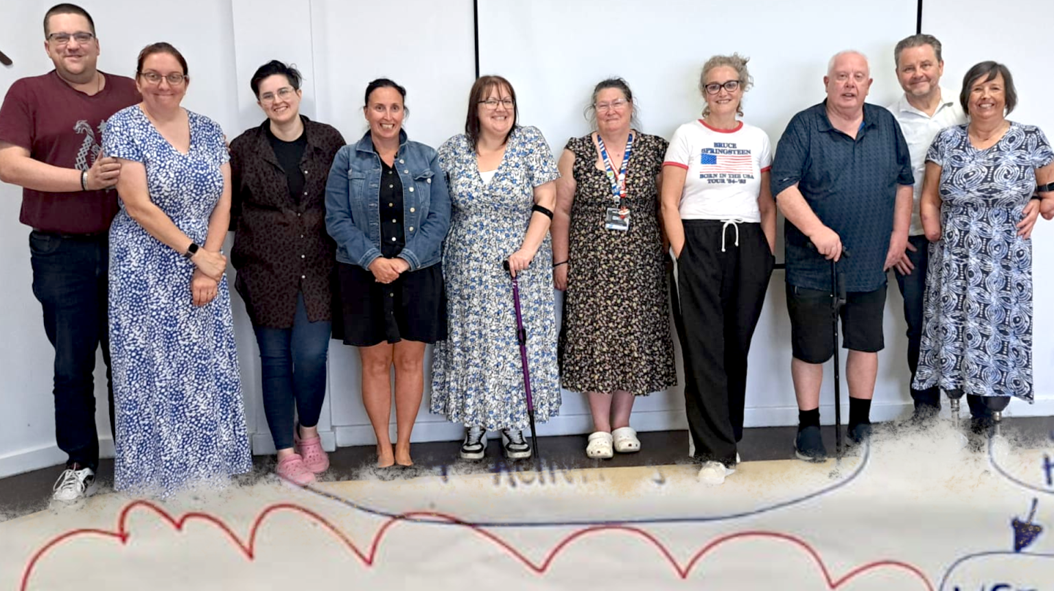 Hartlepool Disability Rights: A group of twelve people stand together, smiling, in front of a white wall at an indoor event. They are of varying ages and genders, some using mobility aids.