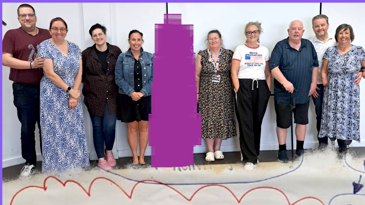 Hartlepool Disability Rights: A group of twelve people stand together, smiling, in front of a white wall at an indoor event. They are of varying ages and genders, some using mobility aids.