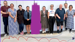 Hartlepool Disability Rights: A group of twelve people stand together, smiling, in front of a white wall at an indoor event. They are of varying ages and genders, some using mobility aids.
