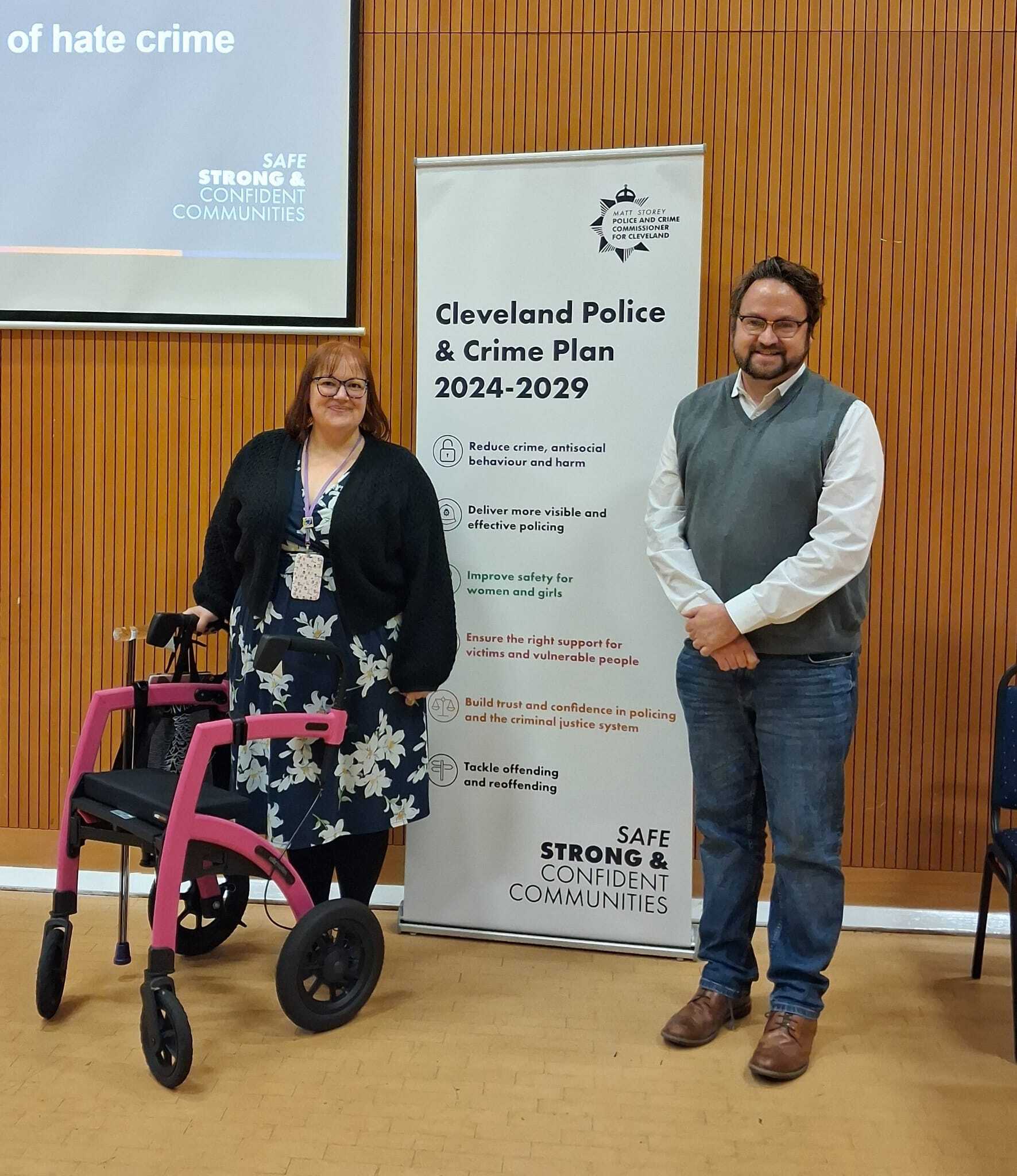 Cleveland Disability Hate Crime: Claire from Difference North East standing with Cleveland Police and Crime Commissioner Matt Storey at the Strategic Hate Crime Workshop, beside a banner showing Cleveland Police and Crime Plan 2024–2029