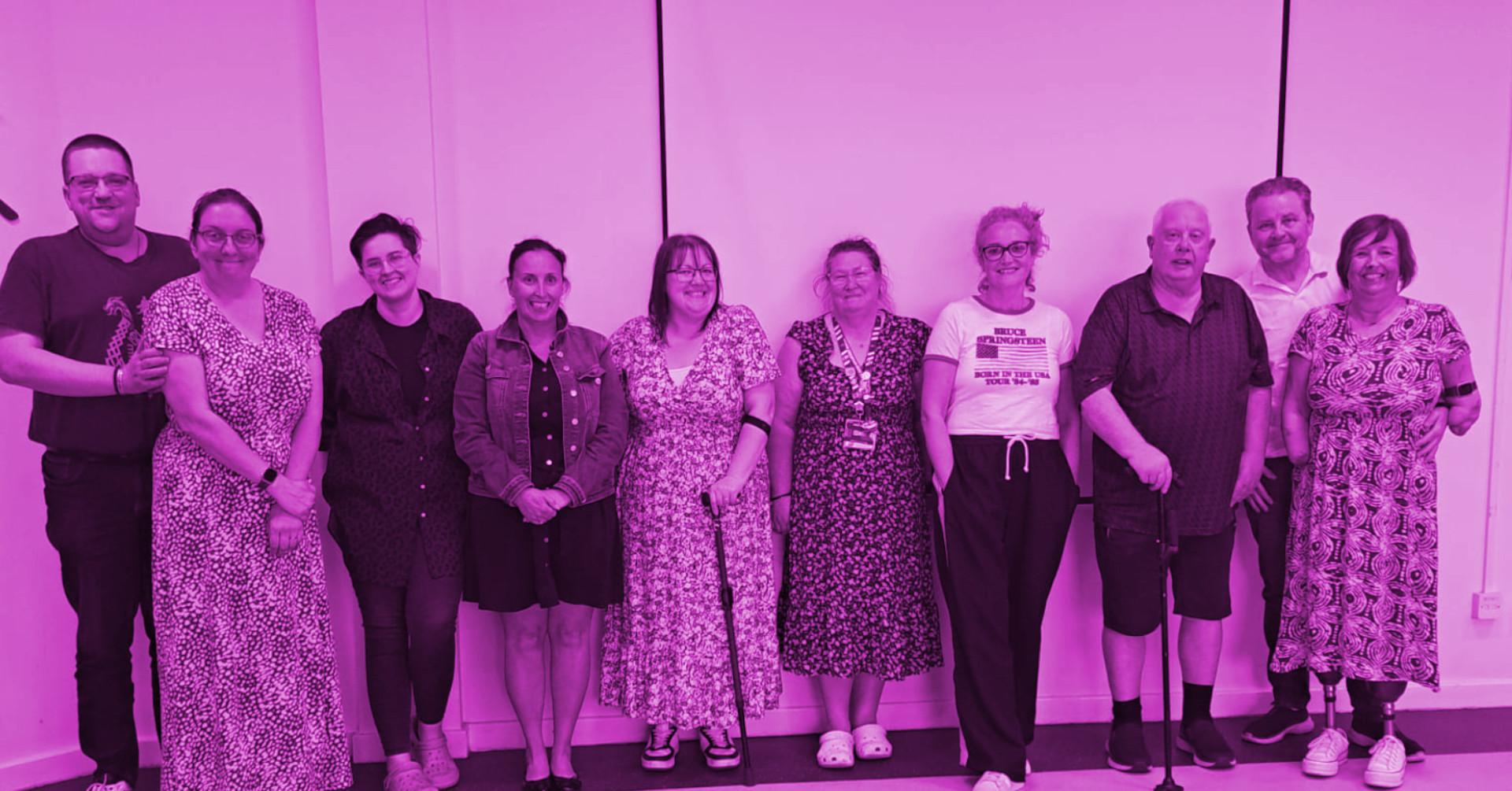 Imagining Accessible Futures - Members' Workshop Amble: A group of ten Difference North East members stand together in a bright room, smiling at the camera. Some people use mobility aids, and everyone appears relaxed and connected. The image has a purple colour overlay, reflecting the colour of the disability movement