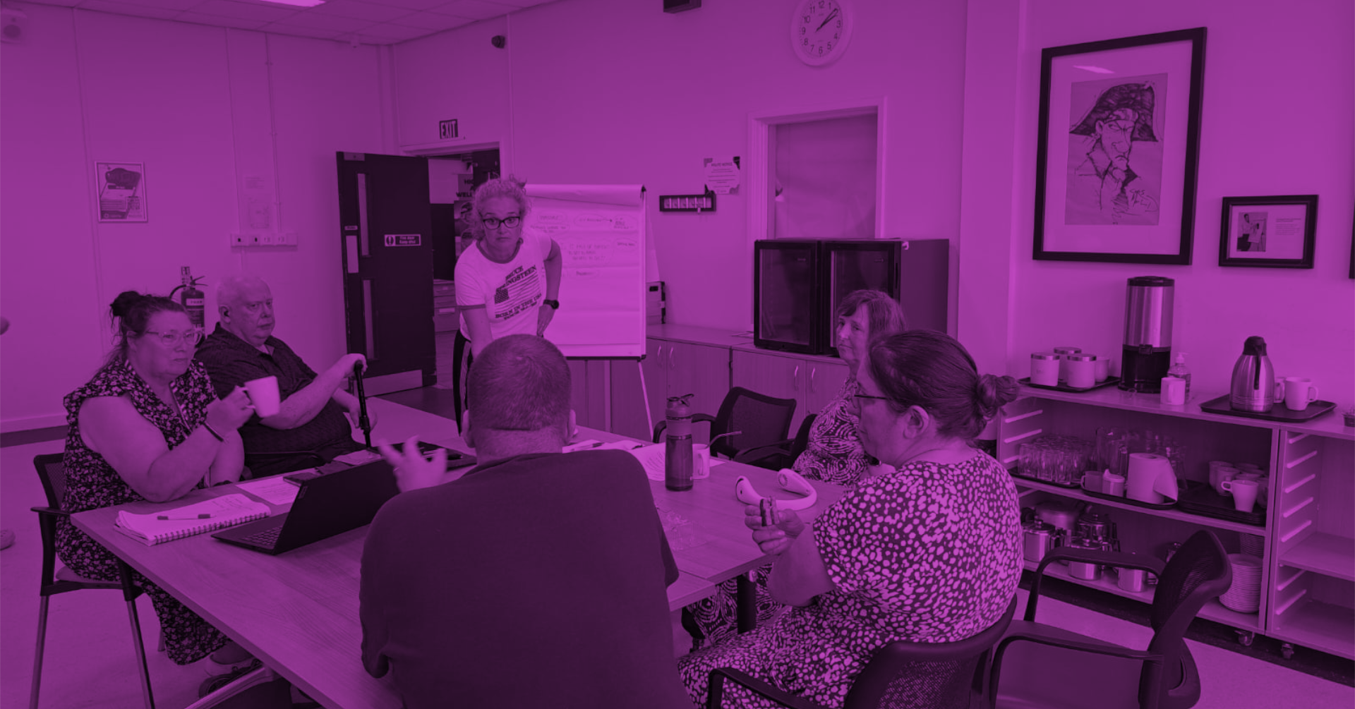 Imagining Accessible Futures - Newcastle City Library. A group of Difference North East members sitting together in a bright room, everyone appears relaxed and connected. The image has a purple colour overlay, reflecting the colour of the disability movement